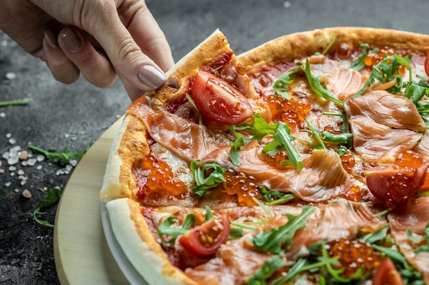 Manos femeninas sosteniendo deliciosa pizza con salmón, caviar rojo, tomates y aragula. pizza italiana.