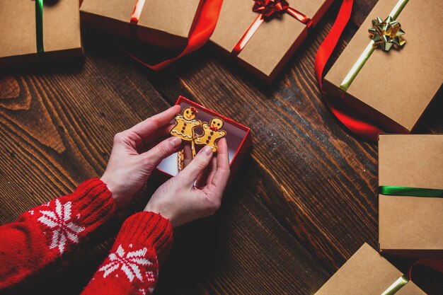 Manos femeninas sosteniendo galletas cerca de cajas de regalo sobre mesa de madera.