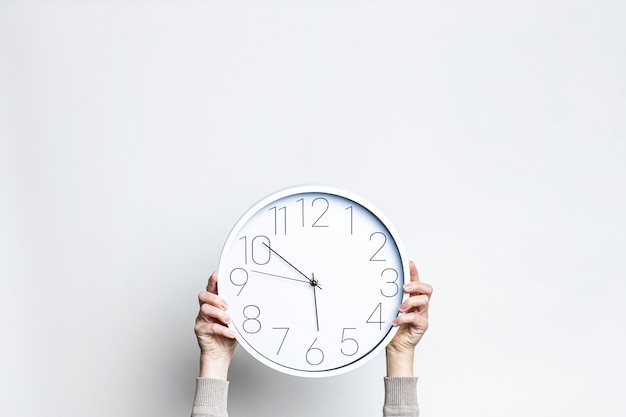 Manos femeninas sosteniendo un gran reloj blanco sobre un fondo claro