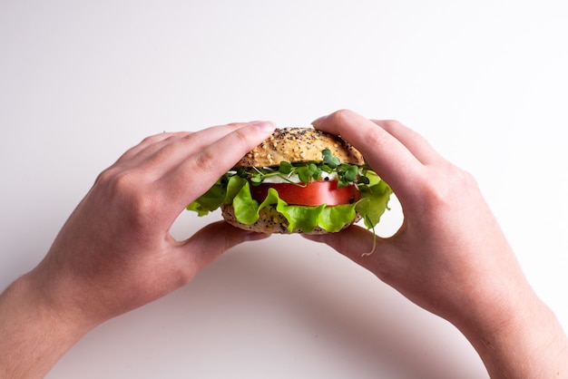 Manos femeninas sosteniendo hamburguesa vegetariana con tomate, queso, lechuga y microgreens