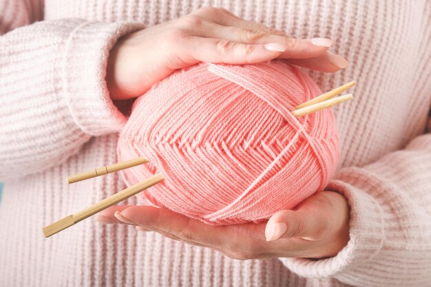 Manos femeninas sosteniendo hilos de lana rosa coloridos y agujas de tejer de madera para trabajos de hobby o arte sobre fondo azul Costura o concepto de tejer Imagen de cierre