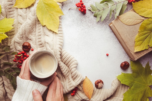 Manos femeninas sosteniendo una manta de café caliente y hojas de otoño sobre fondo de otoño Tonificación vintage concepto de relajación de otoño