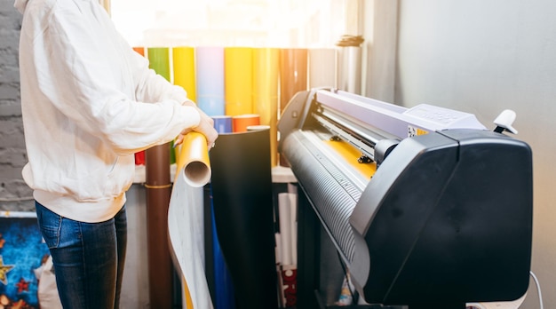 Foto manos femeninas sosteniendo material imprimible amarillo en un plotter de impresión de formato grande diseño gráfico y