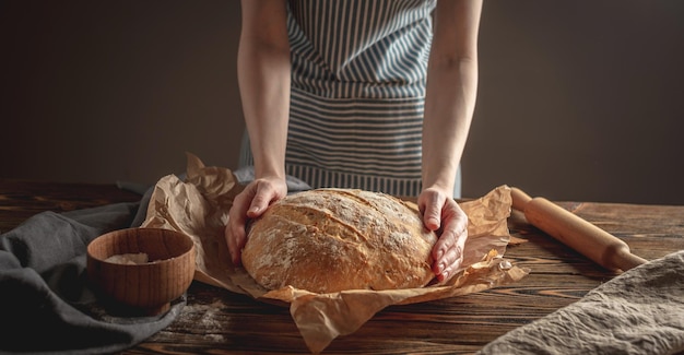 Manos femeninas sosteniendo pan natural casero con una corteza dorada en una servilleta sobre un fondo de madera antiguo Estilo rústico