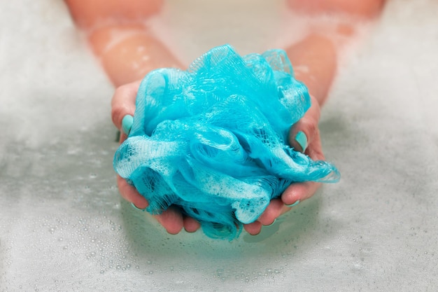 Manos femeninas sosteniendo un paño sintético suave redondo en el baño con agua. Primer plano de las manos. Tratamiento de spa, cuidado corporal, fondo de agua.