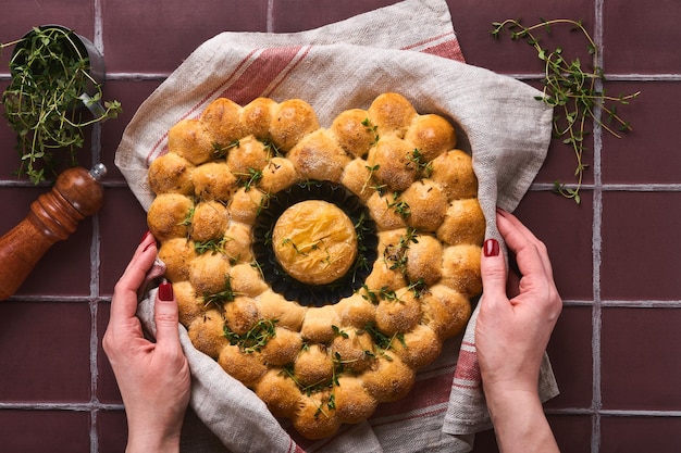 Manos femeninas sosteniendo queso camembert asado y pan casero en forma de corazón y tomillo sobre fondo rústico. Queso francés. Concepto de amor romántico para el Día de San Valentín. Vista superior, copie el espacio.