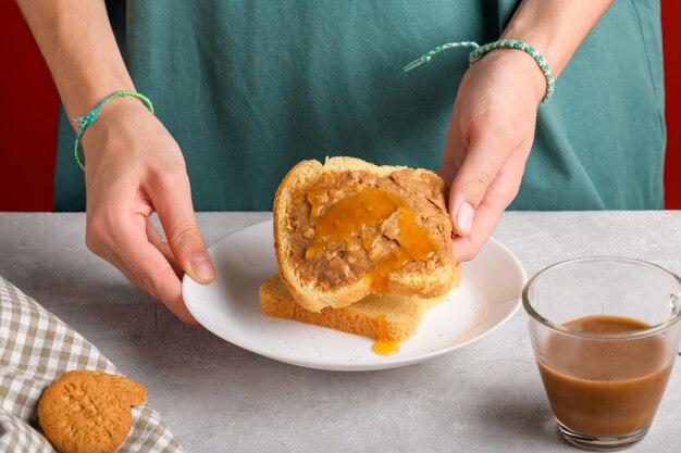 Manos femeninas sosteniendo un sándwich con miel y mantequilla de maní extendida sobre un pedazo de pan blanco