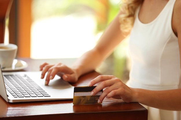 Manos femeninas sosteniendo una tarjeta de crédito con una computadora portátil en la mesa de cerca