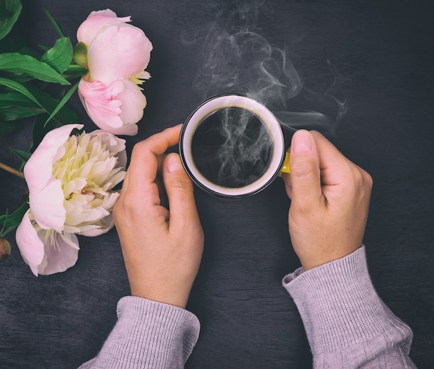 Manos femeninas sosteniendo una taza amarilla con café negro