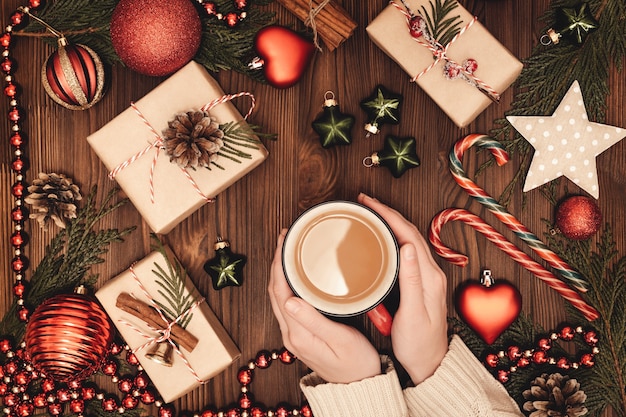 Manos femeninas sosteniendo la taza de café caliente en la mesa de madera con decoración navideña