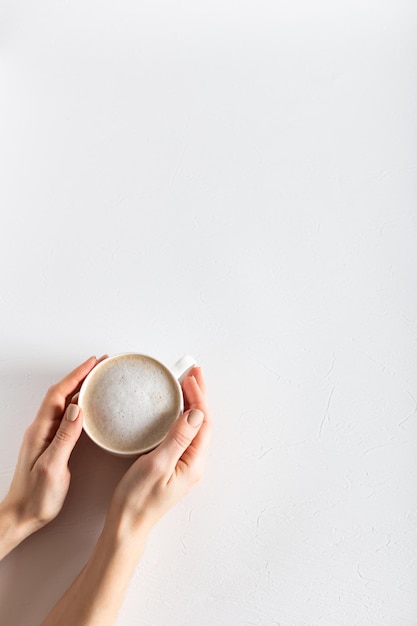 Manos femeninas sosteniendo una taza de café sobre un fondo estructural blanco Espacio de copia