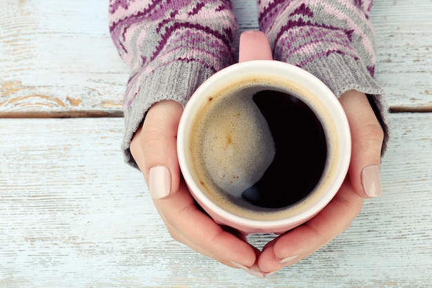 Manos femeninas sosteniendo una taza de café sobre fondo de madera