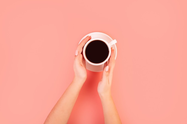 Manos femeninas sosteniendo una taza de filtro de café negro sobre fondo rosa vista superior concepto Flatlay