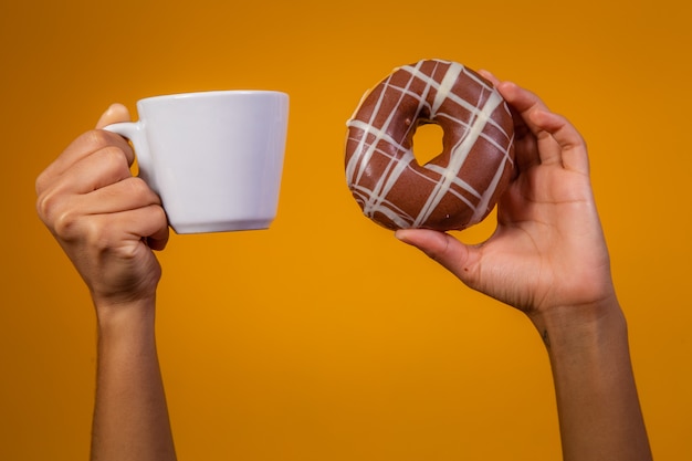 Manos femeninas sosteniendo una taza de leche y donas.