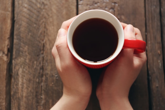 Manos femeninas sosteniendo una taza de té en la mesa de madera