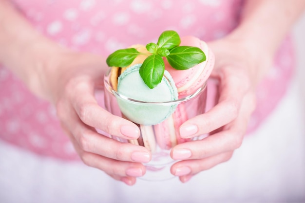 Manos femeninas sosteniendo una taza transparente con macarrones de colores