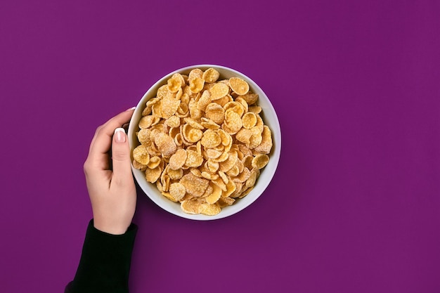 Manos femeninas sosteniendo un tazón con desayuno saludable closeup Tazón con copos de maíz en el fondo colorido