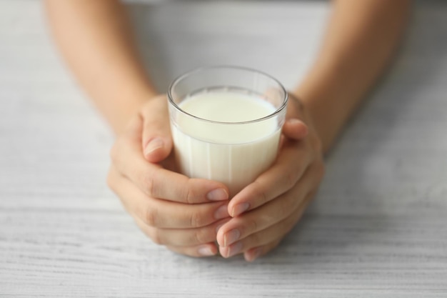 Manos femeninas sosteniendo un vaso de leche fresca sobre fondo de madera clara