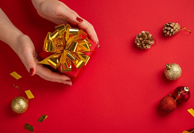 Manos femeninas sosteniendo la vista superior del regalo de Navidad rojo y dorado