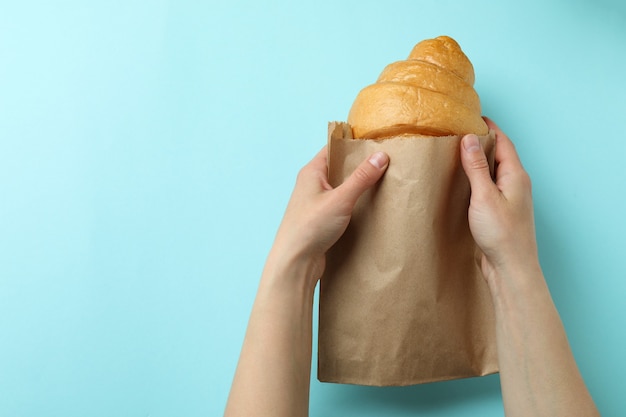 Manos femeninas sostiene una bolsa de papel con croissant en azul