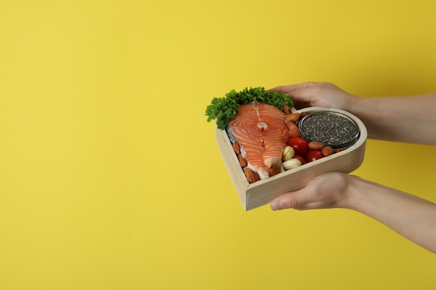 Manos femeninas sostienen alimentos saludables sobre fondo amarillo