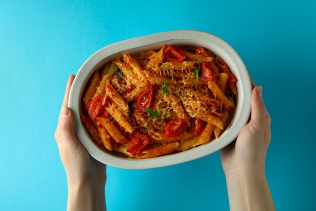 Manos femeninas sostienen la bandeja con pasta con salsa de tomate en azul