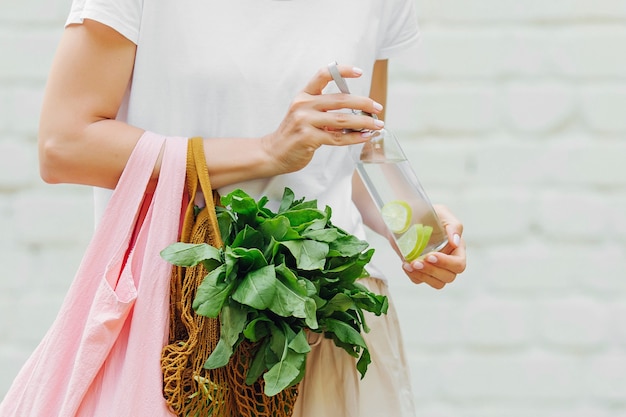 Las manos femeninas sostienen una bolsa ecológica de verduras, verduras y una botella de agua reutilizable. Cero desperdicio. Concepto de estilo de vida sostenible.