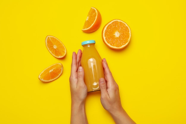 Manos femeninas sostienen una botella de jugo de naranja en amarillo