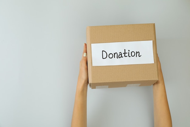 Manos femeninas sostienen caja de donación sobre fondo gris claro