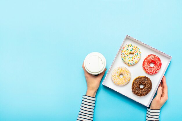 Manos femeninas sostienen una caja con donas, una taza de café en un azul