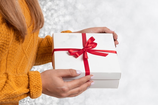 Manos femeninas sostienen una caja de regalo blanca con un lazo rojo