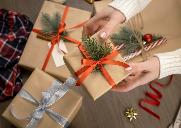 Manos femeninas sostienen caja de regalo con cinta roja y rama de árbol de Navidad en el fondo de la decoración navideña El concepto de preparar regalos para las fiestas