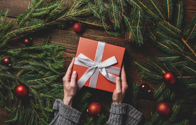 Manos femeninas sostienen la caja de regalo junto a la decoración navideña en una mesa