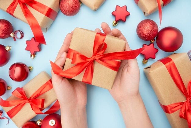 Las manos femeninas sostienen una caja de regalo con un lazo rojo sobre un fondo azul. Fondo de Navidad con adornos y cajas de regalo. Copia de espacio.