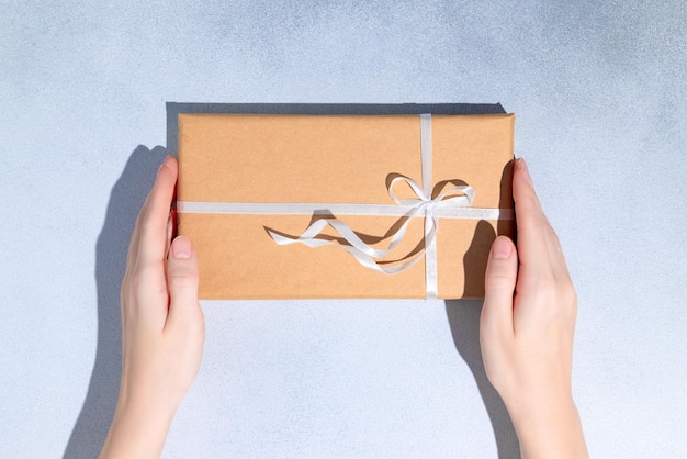 Las manos femeninas sostienen una caja de regalo o un regalo envuelto en papel artesanal. Copiar espacio Mockup Flat lay