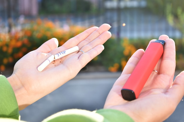 Las manos femeninas sostienen un cigarrillo electrónico en una mano y un cigarrillo de nicotina en la otra.