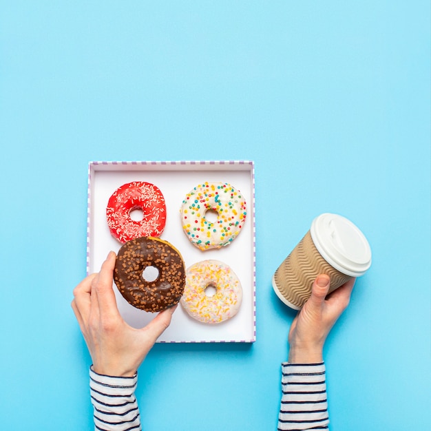 Las manos femeninas sostienen una dona y una taza de café en un espacio azul. concepto de tienda de confitería, repostería, cafetería. bandera.