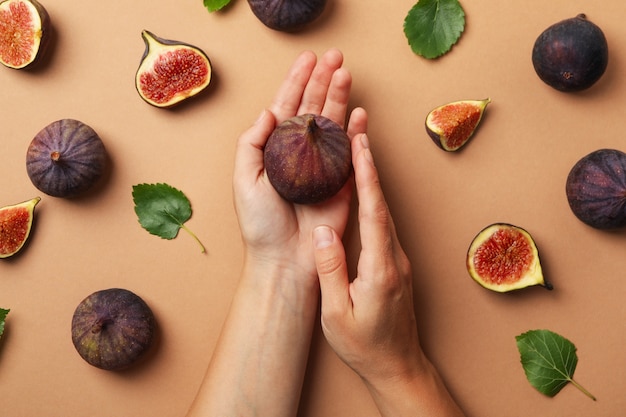 Manos femeninas sostienen higo en artesanía con frutos y hojas de higo, vista superior