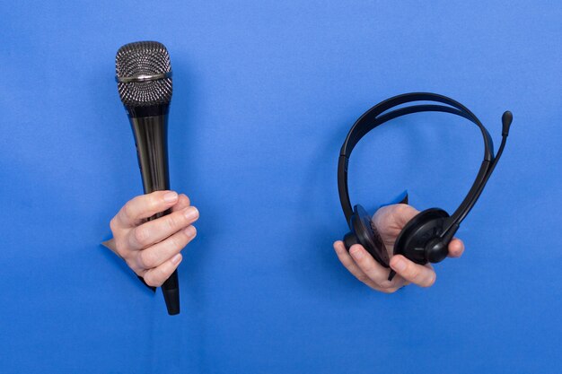 Las manos femeninas sostienen un micrófono y auriculares sobre un fondo azul. Las mujeres se insertan en un fondo de papel. Lugar para una inscripción.