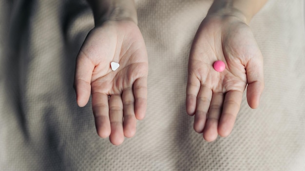 Las manos femeninas sostienen y ofrecen dos cápsulas de píldoras de medicamentos de elección para los dulces o medicamentos blancos y rosados elegidos comparar para elegir Toma de decisiones conceptuales o indecisión