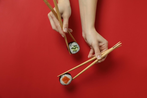 Manos femeninas sostienen palillos con maki sobre fondo rojo.