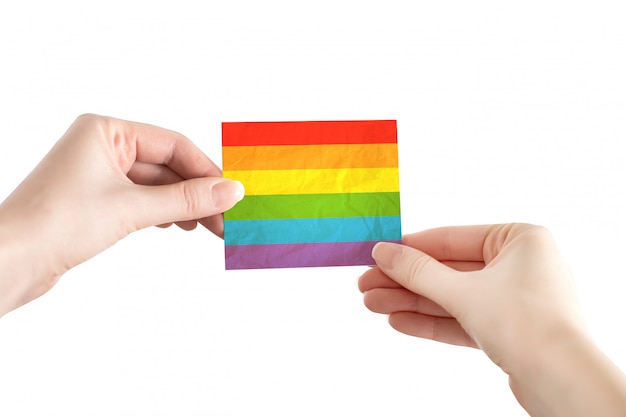 Las manos femeninas sostienen el papel de la bandera LGBT aislado en un fondo blanco, simbolismo, comunidad. Concepto LGBT, día del orgullo. Libertad y derechos de las minorías.