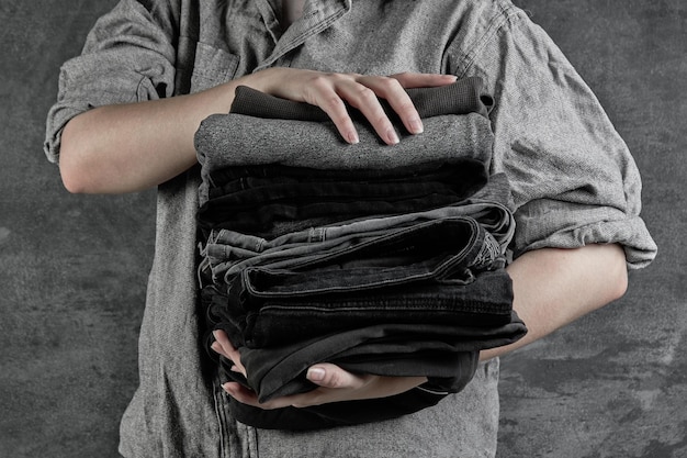 Las manos femeninas sostienen una pila de ropa oscura cuidadosamente doblada aislada en un primer plano de fondo gris negro