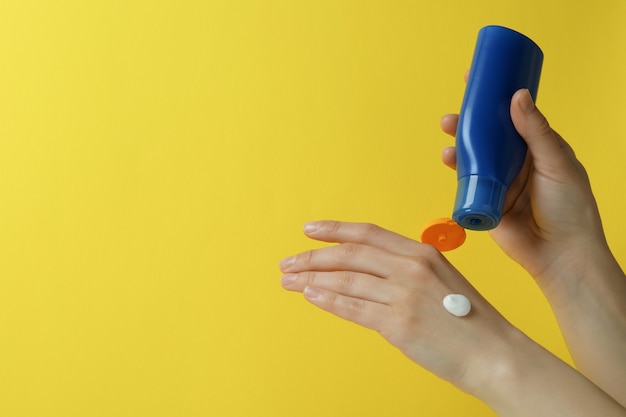 Manos femeninas sostienen protector solar sobre fondo amarillo aislado