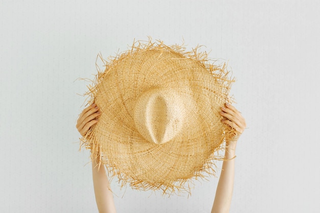 Foto manos femeninas sostienen sombrero de paja de verano sobre fondo blanco.