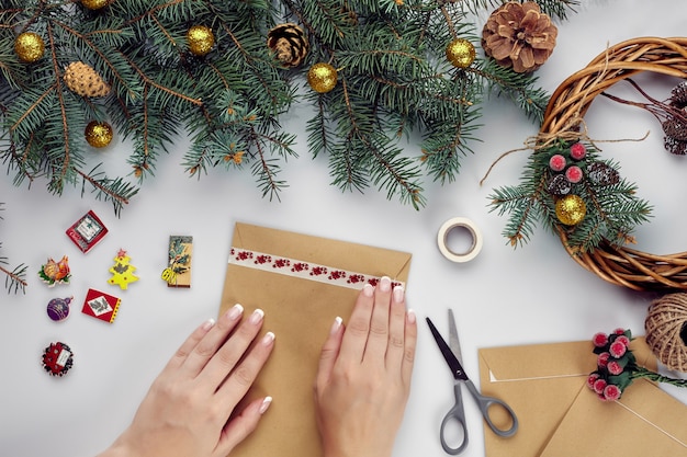 Manos femeninas sostienen tarjeta de feliz navidad y sobre fondo de decoración navideña vista plana endecha superior