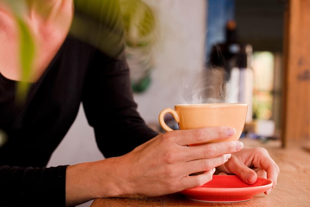 Manos femeninas sostienen una taza amarilla con café se centran en la taza