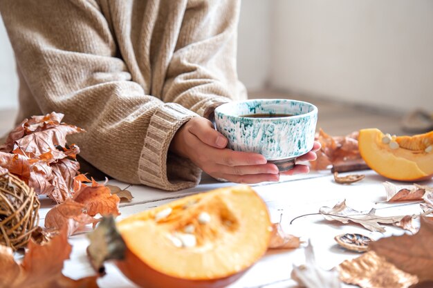 Manos femeninas sostienen una taza de cerámica hecha a mano con una bebida caliente en la pared de la decoración de otoño.