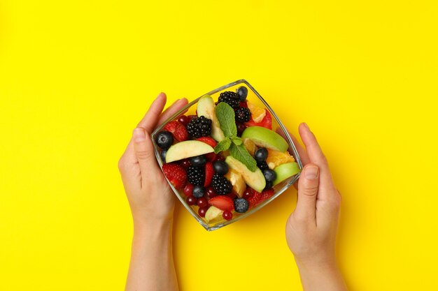 Manos femeninas sostienen tazón de fuente de ensalada de frutas en amarillo