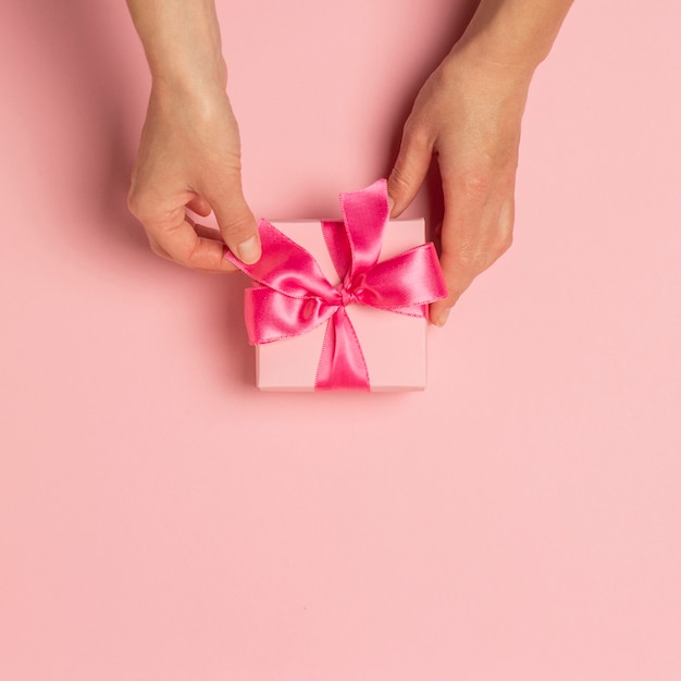 Las manos femeninas sostienen, toman, reciben un regalo en una superficie rosada. día de San Valentín